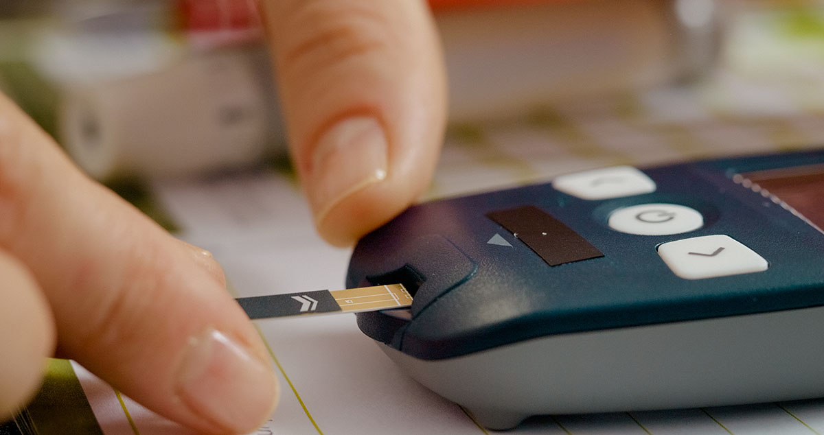 Femeie introduce cu atentie banda de test intr-un aparat pentru glicemie