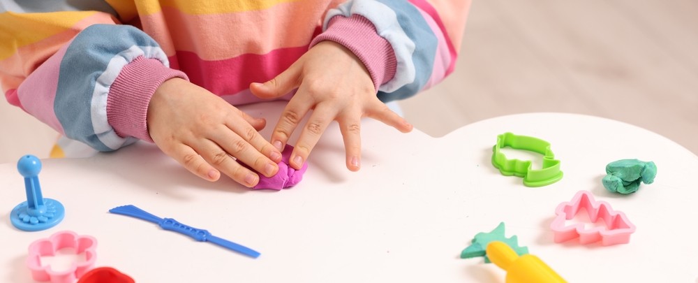 Mainile unei fetite ce se joaca cu plastilina