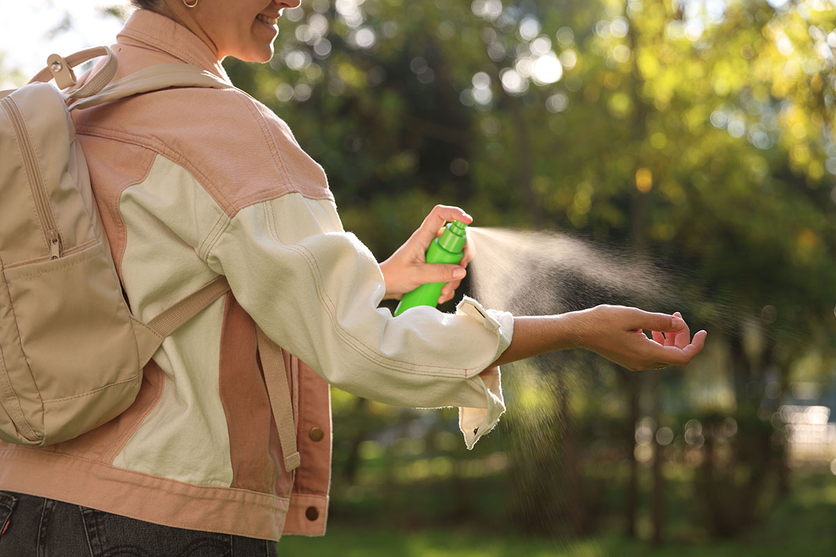 Femeie aplicand spray anti-capuse pe mana in timpul unei drumetii.