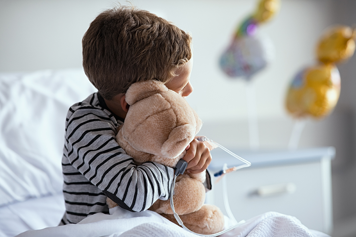 Copil internat la spital cu branulă care ține ursuleț de pluș în brațe