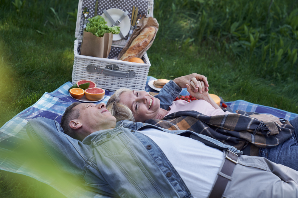 Cuplu matur relaxat sta intins pe iarba si se bucura de un stil de viata sanatos