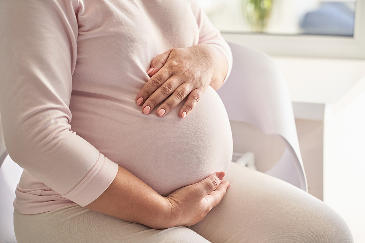 Femeie insarcinata sta pe canapea si isi atinge burtica