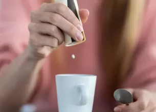 Femeie care arunca pastile de zaharina pe o ceasca de cafea in bucatarie acasa