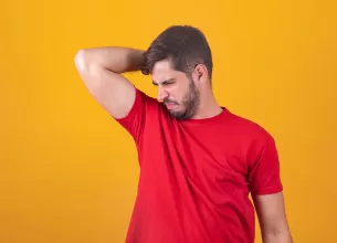 Bărbat în tricou roși mirosindu-și subrațul, deranjat de mirosul neplăcut al corpului.