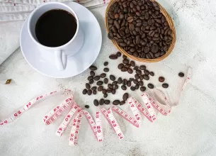 Cana de cafea neagra pe masa, cu boabe de cafea si o banda pentru masurat langa.