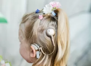 Copil cu spatele, purtand un implant cohlear si un aparat auditiv