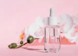 Sticla transparenta cu pipeta care contine ser cosmetic cu panthenol pe fundal roz pastel