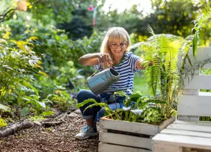 Femeie matura care uda plantele din gradina ei, bucurandu-se de ingrijirea florilor si de timpul petrecut in aer liber