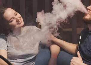 Cuplu in care ea il priveste pe el fumand narghilea