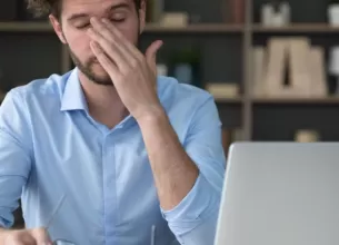 Barbat care lucreaza la biroul de acasa si care a luat o pauza de la privitul la laptop pentru a-si relaxa ochii obositi