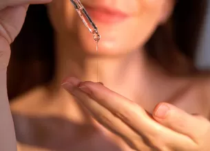 Mainile unei femei care isi aplica ulei de batana in palma cu o pipeta