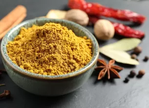 Pudra de curry intr-un bol, cu alte condimente in jur.