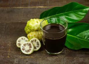 Suc de noni in pahar transparent, cu fructe noni langa.