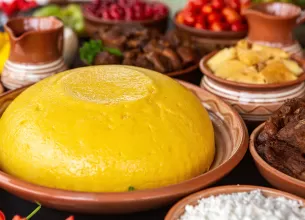 Mamaliga rasturnata pe o farfurie, langa farfurii cu carne si branza