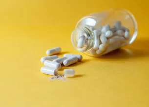 Recipient de sticla deschis cu capsule si pastile imprastiate pe suprafata