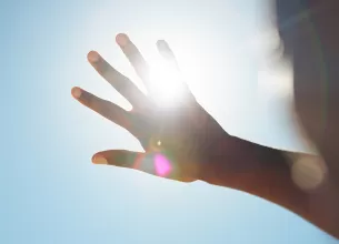 Persoana incercand sa blocheze lumina soarelui cu mana.