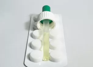 Pipeta de laborator asezata deasupra unor pastile albe
