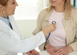 Cardiolog cu stetoscop, ascultand bataile inimii unui pacient la o masa din cabinet