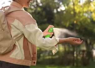 Femeie aplicand spray anti-capuse pe mana in timpul unei drumetii.