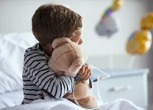 Copil internat la spital cu branulă care ține ursuleț de pluș în brațe