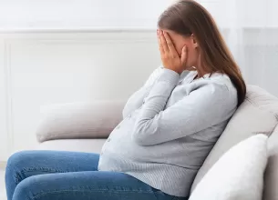 Femeie insarcinata plangand si acoperindu-si fata cu mainile