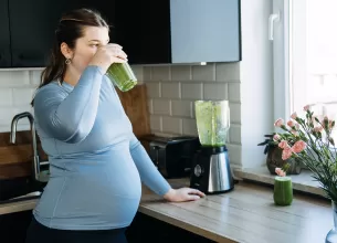 Femeie insarcinata prepara un smoothie verde in bucatarie