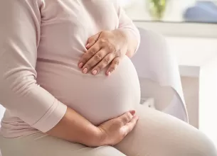 Femeie insarcinata sta pe canapea si isi atinge burtica