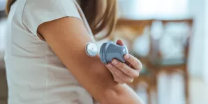 Femeie care isi aplica un senzor de monitorizare a glucozei pe brat, utilizand un dispozitiv pentru diabet