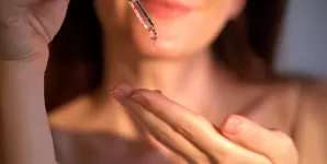 Mainile unei femei care isi aplica ulei de batana in palma cu o pipeta