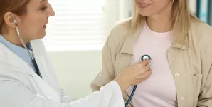 Cardiolog cu stetoscop, ascultand bataile inimii unui pacient la o masa din cabinet