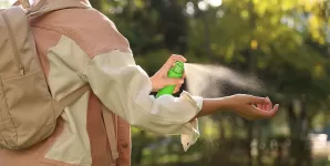 Femeie aplicand spray anti-capuse pe mana in timpul unei drumetii.
