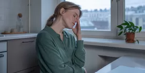 Femeie obosita care sta la masa langa laptop dupa o zi solicitanta