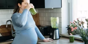 Femeie insarcinata prepara un smoothie verde in bucatarie