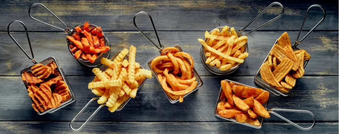 Diferite tipuri de cartofi prajiti in cosulete din metal, pe o masa din lemn inchis la culoare