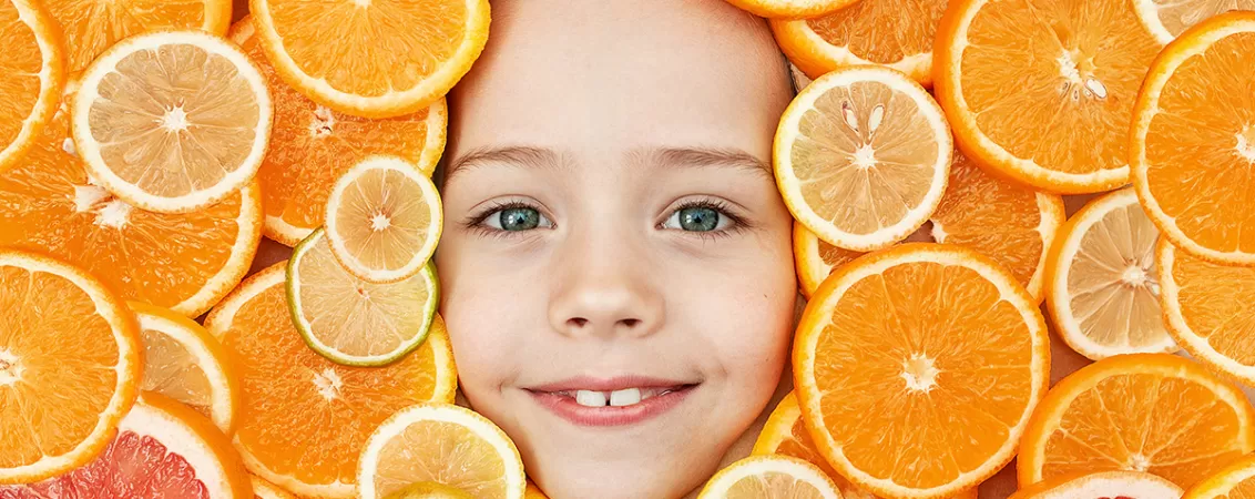 Fata unui copil inconjurata de felii de portocale si alte citrice care contin vitamina C