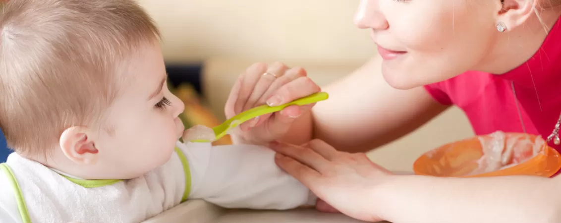 Femeie tanara isi hraneste copilul mic cu cereale de bebelusi