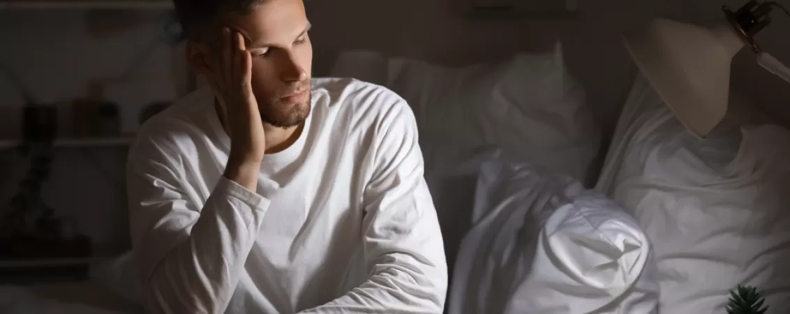 Barbat suferind de insomnie, stand pe marginea patului in timpul noptii