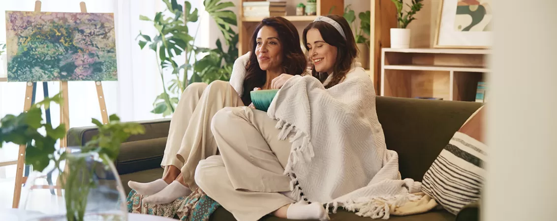 Mama si fiica stand pe o canapea si uitandu-se la TV