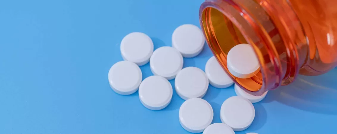 Antiinflamatoare sau medicamente pentru durere pe un fundal albastru, lângă o sticlă medicinală.