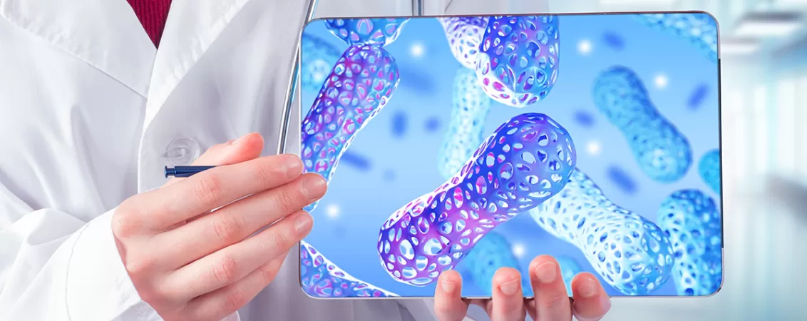 Doctor recomandand probiotice, aratand spre o tableta cu o ilustratie a celulelor microbiotei intestinale colorate