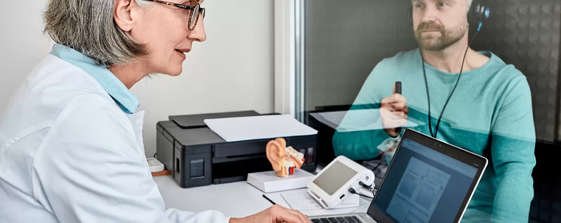 Femeie medic efectuand o audiograma unui pacient barbat in cabinetul medical cu echipament special