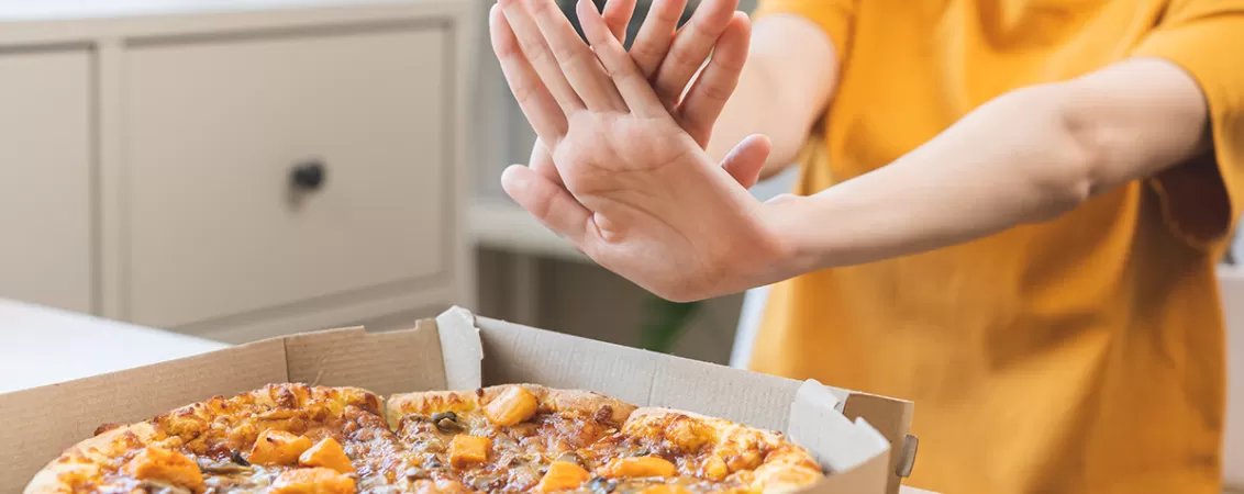 Femeie refuzand sa manance o pizza care contine multi carbohidrati