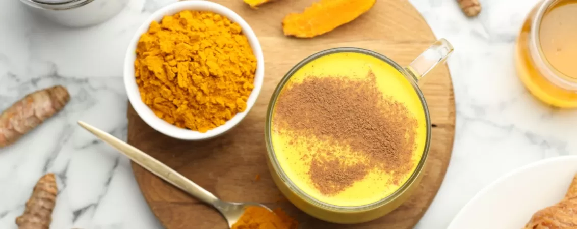 Cana de turmeric latte langa pudra turmeric si rizomi
