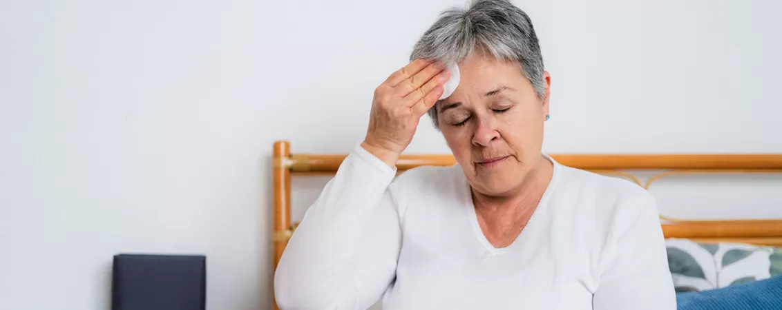 Femeie la menopauza folosind o discheta din bumbac pentru a sterge transpiratia rece de pe frunte. 