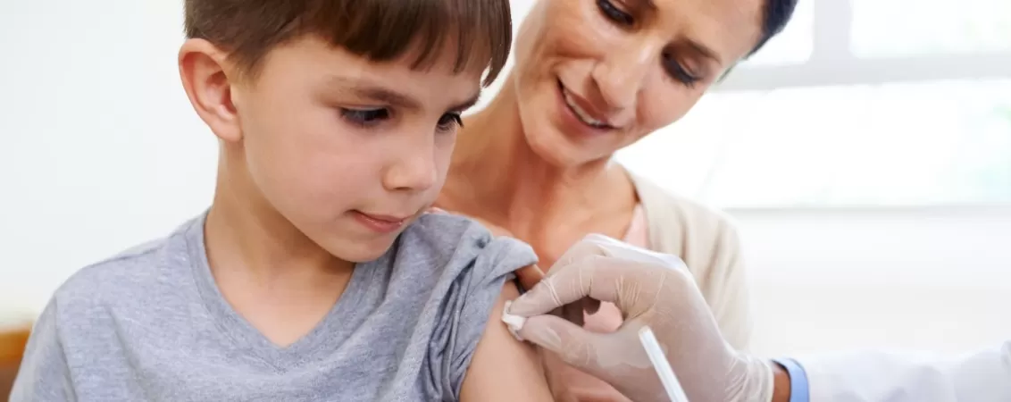 Medic se pregateste sa vaccineze un baietel tinut in brate de mama lui 