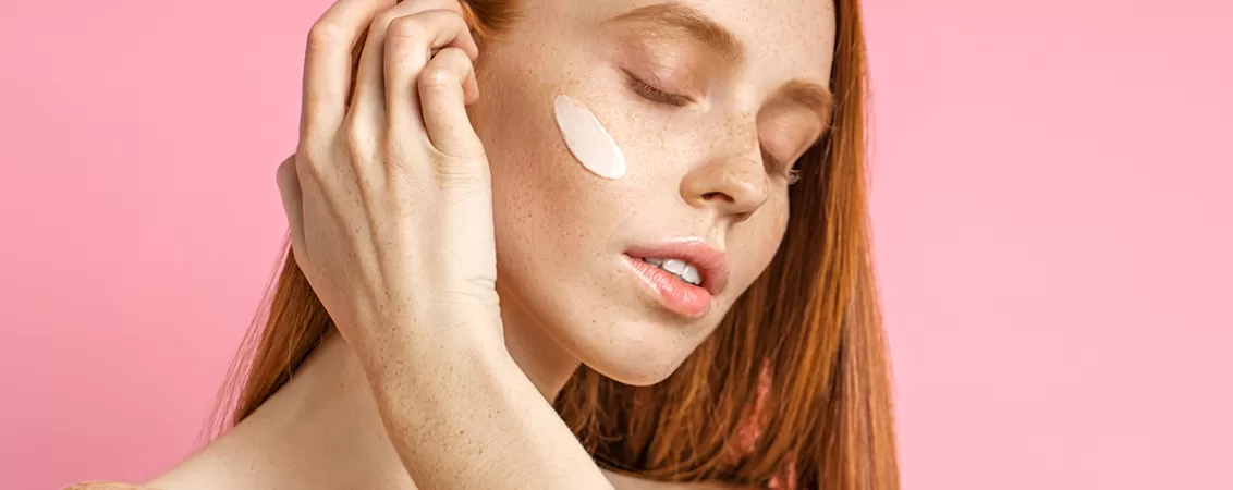 O tanara roscata aplica un produs de ingrijire a pielii pe tenul sensibil