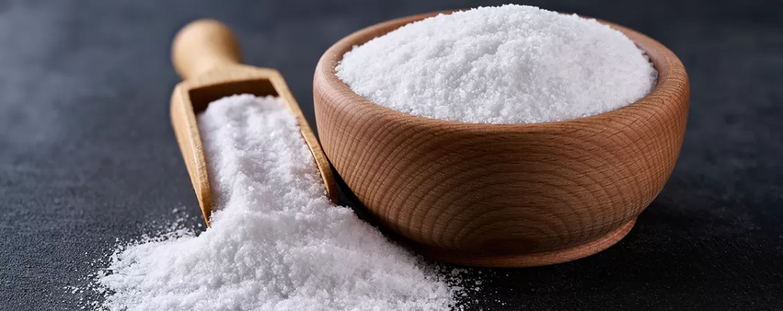 Sare intr-un bol din lemn, pe o masa inchisa la culoare.