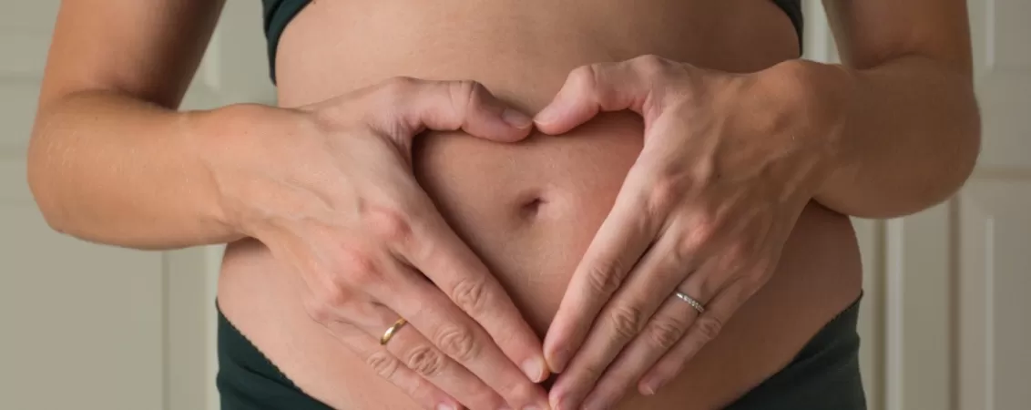 Femeie insarcinata care formeaza o inima cu mainile pe burtica