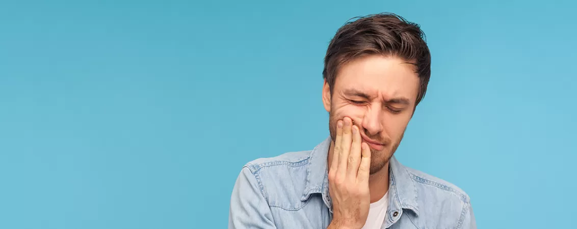 Bărbat exprimă dureri dentare, pe fundal albastru