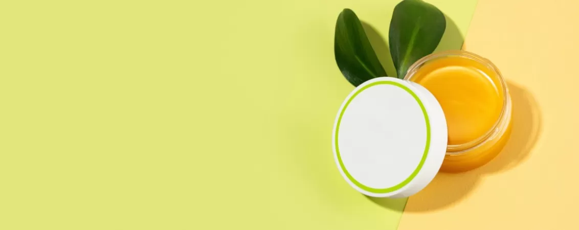 Cutie deschisa cu balsam pe baza de lanolina, asezata pe o suprafata galbena si verde pal